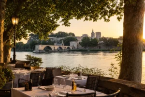 Restaurant terrace by the Rhône in Avignon at sunset with views of the river and historic landmarks.