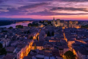 Vue panoramique du centre historique d'Avignon à l'heure bleue, avec le Palais des Papes et les toits en terrasse éclairés pa